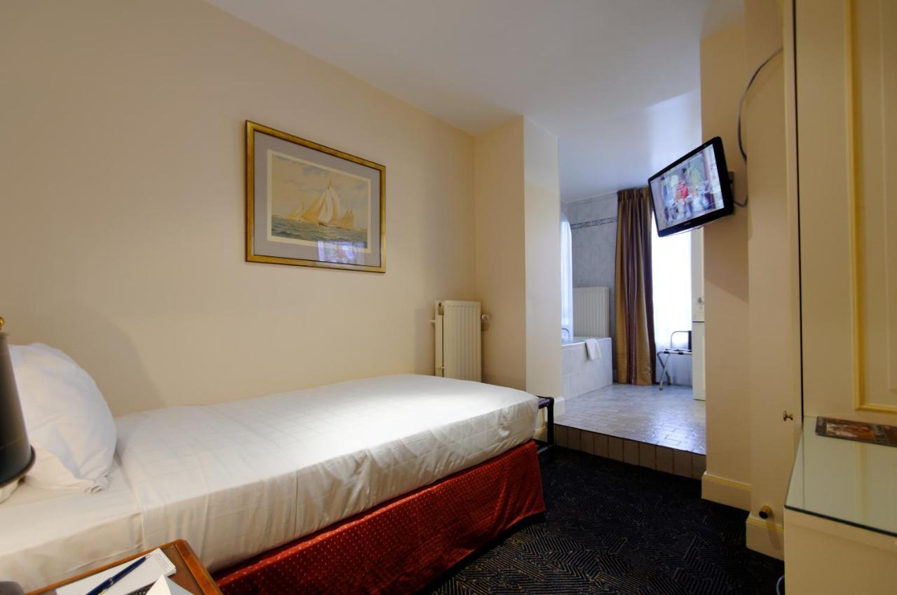 Hotel Le Plaza Brussels Exterior photo The photo shows a small hotel room featuring a single bed with white linens and a dark red bed skirt. There's a painting on the wall above the bed. A flat-screen television is mounted on the wall across from the bed. To the right, there's a doorway t